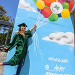 Graduate in cap and gown in front of a balloon mural at the parking structure