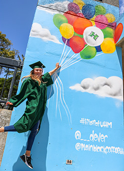 Graduate in cap and gown in front of a balloon mural at the parking structure