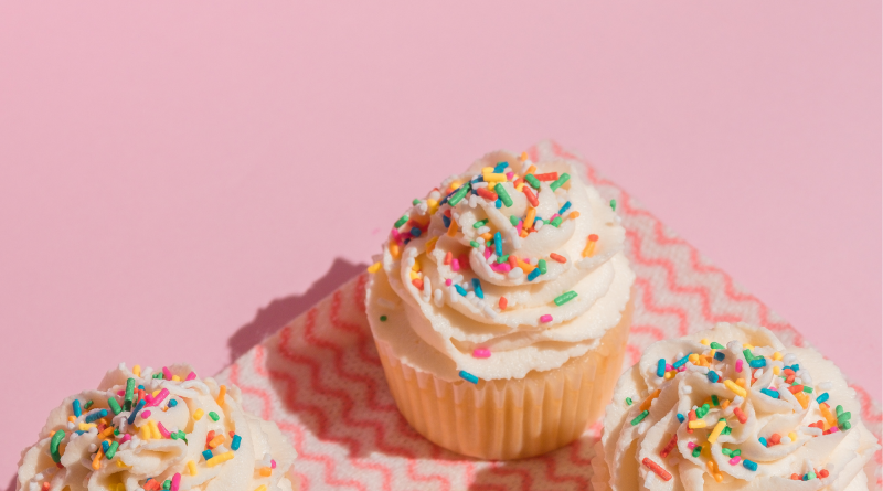 pink background with cupcakes with white icing and sprinkles