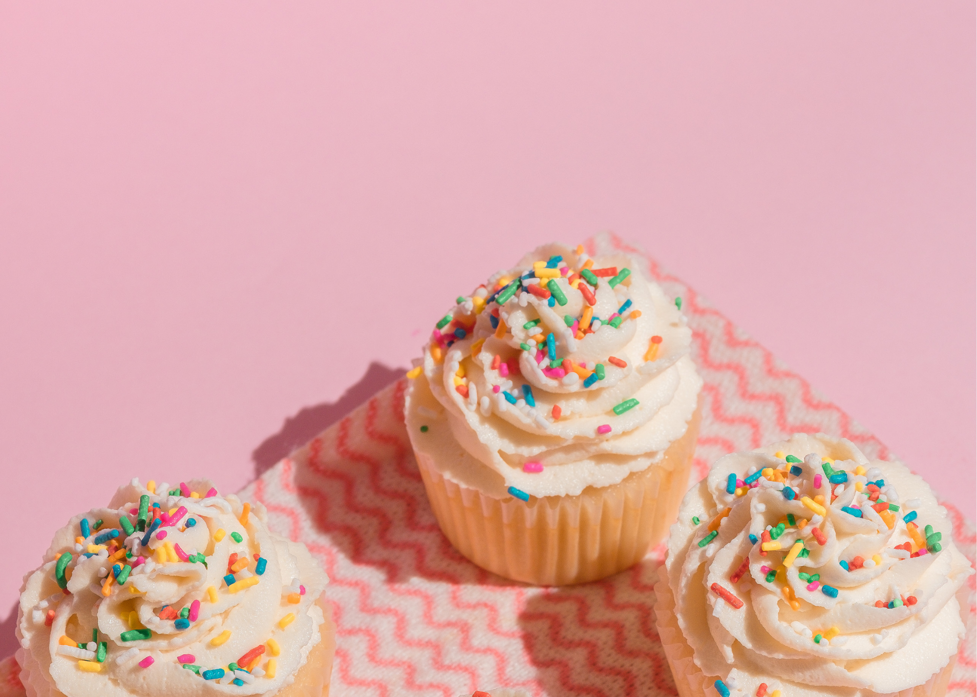 pink background with cupcakes with white icing and sprinkles