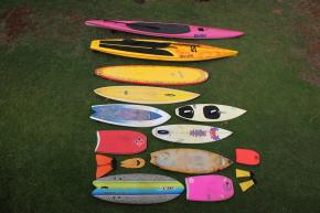 <p><strong>SF Fig. 4.2.</strong> (<strong>B</strong>) A versatile surf quiver can include many types of crafts, for example the quiver shown here includes a 14’ prone paddleboard, a 12’6” standup paddleboard and paddle, a 9’ long board, a 8’ gun surfboard, a 5’8” tow surfboard with straps, a 5’8” fish surfboard, s 5’9” shortboard, s 3’6" body board, s 6’ retro fish surfboard, s 1.5’ mini body board, orange surf fins, s wooden hand plane for body surfing, s 6’5” foam fish surfboard, s 3’1” bodyboard, and yellow surf fins.</p>

