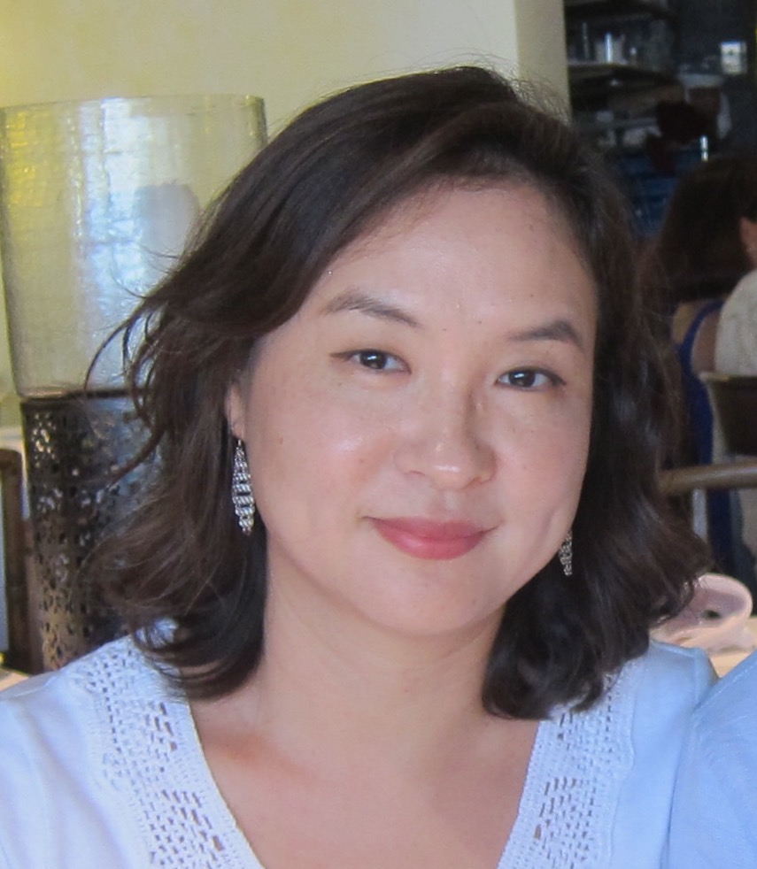 Dr. Park wearing a white garment, dangling earrings and reddish-pink lipstick.