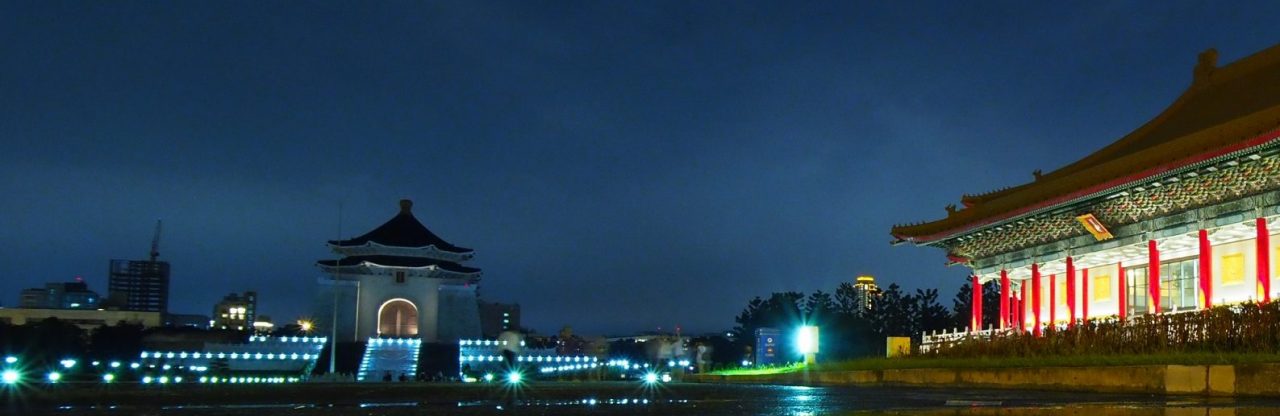 Left side contains Chiang Kai-shek memorial, white building with blue rooftop and blue-lights on stairs. Right side has Chinese-style building with red pillars, green decoration and orange rooftop lit up. Background is dark gray sky with white clouds.