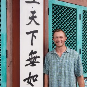 A Man Standing By A Building With Blue Windows And Writing In Chinese