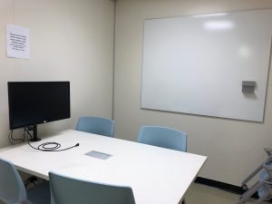 a group study room with 4 chairs, a table, monitor, and whiteboard