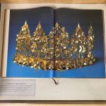 A book open to an image of a gold crown on blue background from the Afghanistan: “Graveyard” of Empires Exhibit 1 of 5