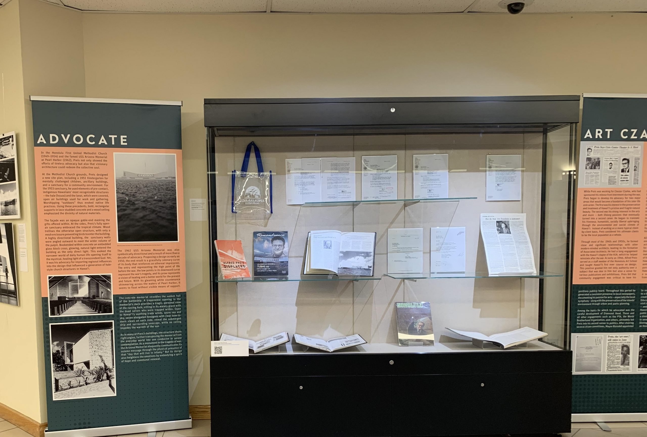 Pries Exhibit - Books in display case and banner titled Advocate