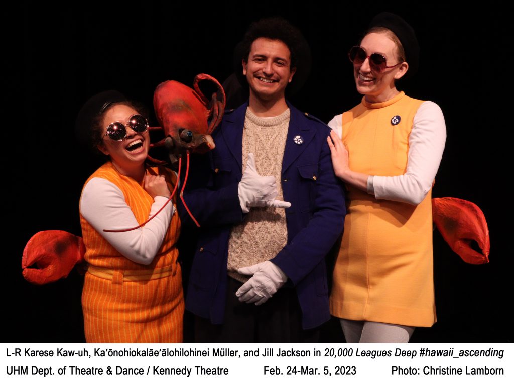 3 college actors holding a giant lobster, 2 wearing matching outfits. Text: L-R Karese Kaw-uh, Jill Jackson, and Ka’ōnohiokalāe’ālohilohinei Müller in 20,000 Leagues Deep #hawaii_ascending. UHM Dept. of Theatre & Dance / Kennedy Theatre           Feb. 24 - Mar. 5, 2023                  Photo: Christine Lamborn.