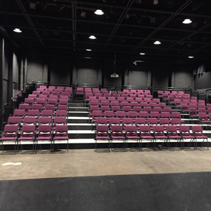 View Of Lab Theatre Audience Chairs From The Stage. Each Row Of Chairs Is One Step Up. Eight Rows In Three Sections Divided By 2 Aisles: 4 Chairs, 8 Chairs, 4 Chairs. Last Row Is 19 Chairs, No Aisles.