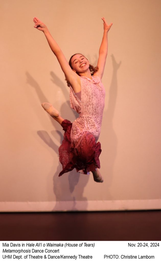 Smiling female dancer in lace ombre dress mid-leap with arms above head smiling at camera.