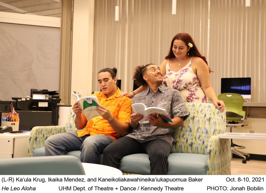 Color photo of three students in NHSS lounge on UHM campus. Two males are sitting on couch with female standing behind looking over their shoulders. Caption under photo reads, "(L-R) Ka‘ula Krug, Kaneikoliakawahineika‘iukapuomua Baker, and Ikaika Mendez. Oct. 8-10, 2021. He Leo Aloha. UHM Dept. of Theatre + Dance / Kennedy Theatre. PHOTO: Jonah Bobilin."