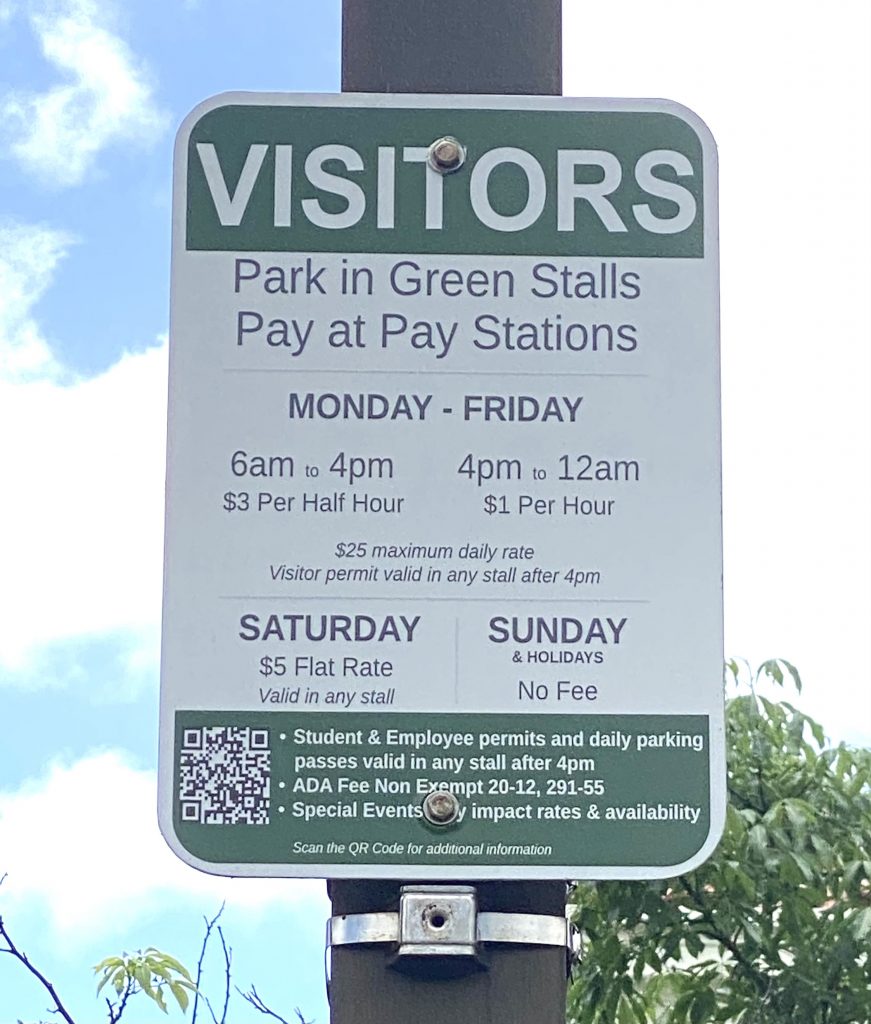 Parking sign on pole. Text reads " Visitors park in green stalls. Pay at Pay stations. Monday-Friday 6am to 4pm $3 per half hour. 4pm to 12am $1 per hour. $25 maximum taily rate. Visitor permit valid in any stall after 4pm. Saturday $5 flat rate valid in any stall. Sunday & holidays no fee. Student & Employee permits and daily parking passes valid in any stall after 4pm. ADA Fee Non Exempt 20-12, 291-55. Special Events may impact rates & availability."