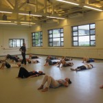 Students in dance classroom lying on floor with instructor walking around