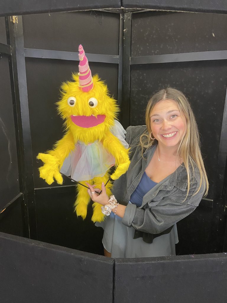 Photo of Olivia Coughlin with yellow puppet smiling at camera