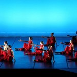 Photo from dance concert with dancers sitting on ground reaching out in front of them