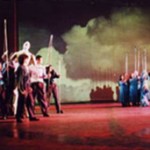 Group of performers in two separate clumps holding tall rods