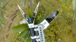 The device consists of a rotating chainsaw with a robotic gripper claw mounted beneath the drone.