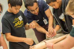 A UH medical student leads teens in stitching up a wound at JABSOM's Teen Health Camp 2017.