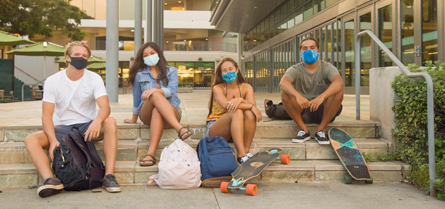 photo of 4 students with their backpacks sitting on a stairs at Campus Center wearing masks