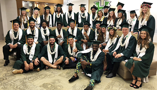 photo of 3 rows of student athletes in their cap and gowns, sash, and leis in the Nagatani Center