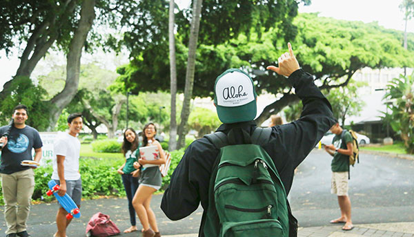 a male student wave shaka to signal aloha to other four students nearby