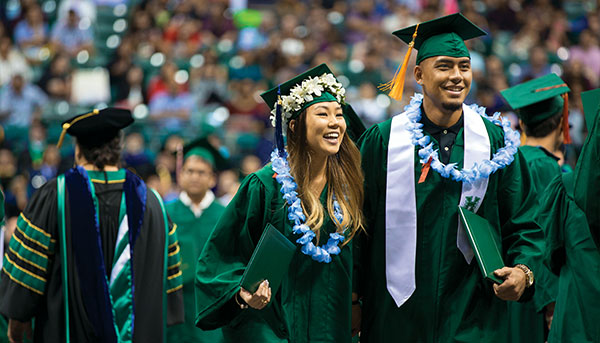 two students in green gown at graduation ceremony