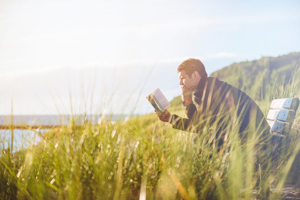 Male student reading a book on next to the ocean