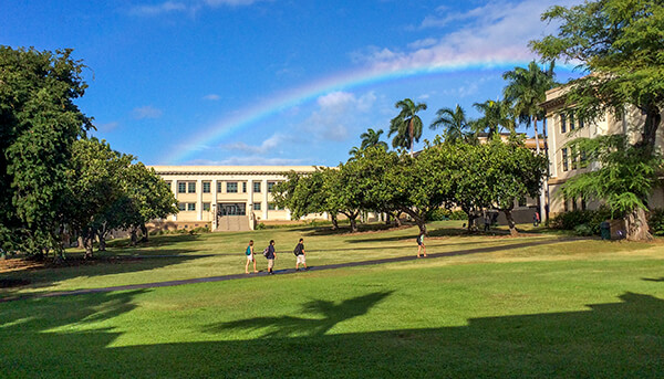 The Manoa Quad with students in the foreground and a rainbow in the background