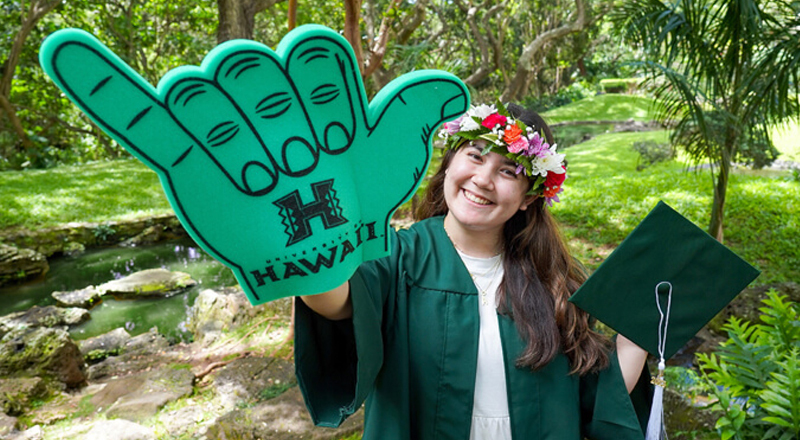 Student wearing commencement attire with a big shaka