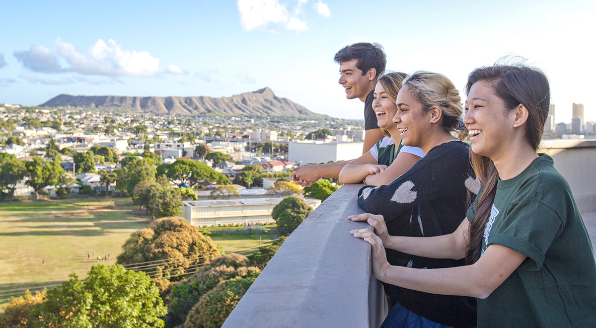 Four smiling students on a rooftop with Diamond Head in the background